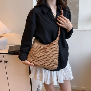 Dettaglio di borsa tote in paglia intrecciata a mano con tracolla in pelle marrone