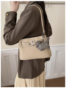 Detalle de bolso de cuero granulado con cierre plateado y colgante de caballo gris elegante