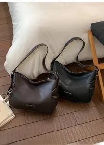 Minimalist leather crossbody bags in dark brown and black on a wooden floor
