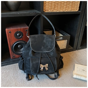 Detail of black suede backpack with gold bow accent and drawstring closure