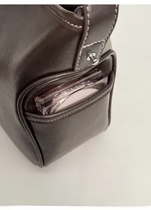 Detail of the brown leather tote bag side pocket holding a round cosmetic compact