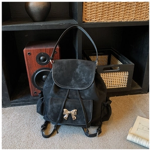 Detail view of black vintage backpack featuring a gold bow buckle on the front pocket