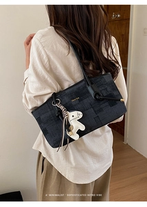Détail du sac Boston noir avec logo doré, texture denim et accessoire de charme de cheval