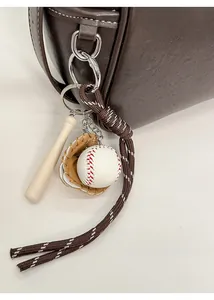 Detail of a baseball glove and bat keychain accessory hanging on a brown leather tote bag