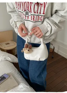 Close-up of white pleated cloud bag with a cute brown teddy bear charm on model