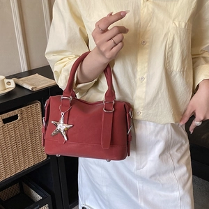 Detail of red leather Boston bag with a silver starfish pendant held by a model