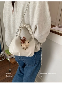 Detail of off-white pleated handbag featuring a plush bear charm and silver chain strap