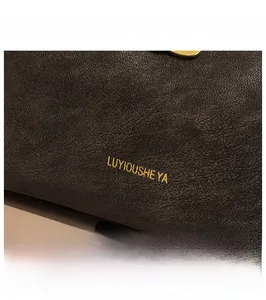 Nahaufnahme der dunkelbraunen Leder-Handtasche mit goldenem Logo und feiner Narbung