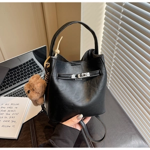 Detail of black leather bucket bag with silver buckle and cute brown plush bear charm