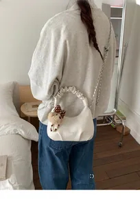 Detailed view of white pleated handbag with bear charm and silver chain strap