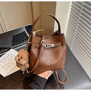 Detail of a brown leather bucket bag featuring a silver buckle and cute bear pendant