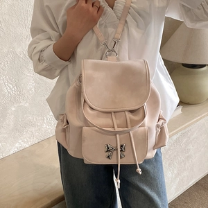 Detail of light pink backpack with matte finish and metallic bow decoration on front pocket
