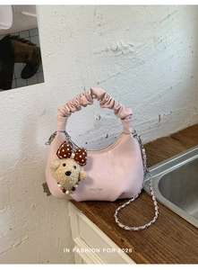 Detail of light pink crescent handbag with cloud pleated handle and plush puppy pendant