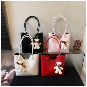 Detail view of four glossy leather tote bags in black, pink, cream, and red with bear charms