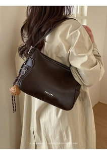 Detail of dark brown leather shoulder bag with silver logo and heart charm accessory