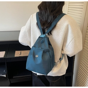 Dunkelgrüner Nylon-Rucksack mit Kordelzug und Metall-Logo am Rücken des Models getragen