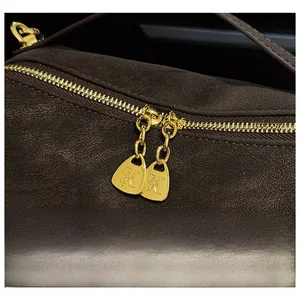 Detail von goldenen Doppelreißverschlüssen mit K-Logo auf einer braunen Ledertasche