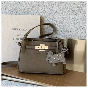 Detalle de bolso de cuero caqui con cierre de metal giratorio y colgante de caballo decorativo