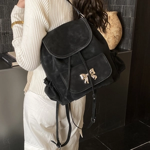 Detail of black matte backpack featuring gold bow accent and ruffled lace edge