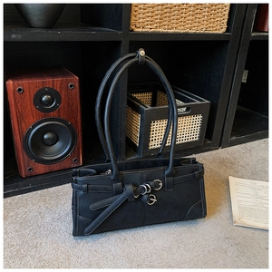 Close-up of black matte leather handbag with belt straps and silver ring accents