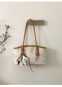 Détail d'un sac cabas beige avec lanières en cuir et un petit charm de cheval
