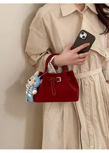 Detail of burgundy suede handbag with decorative buckle and cute plush bear charm accessory