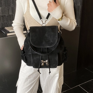 Close-up of black suede backpack featuring a stylish silver metal bow and side pockets
