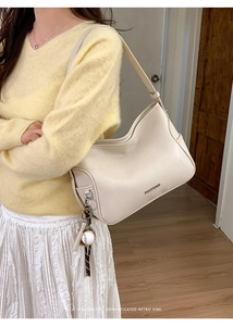 Detail of minimalist cream tote bag with metal logo and unique baseball charm accessory