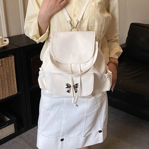Front view of white leather backpack featuring a metallic bow and flap closure on a model