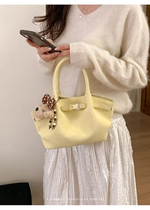 Primer plano de un bolso tote de cuero amarillo pálido con hebilla y charm de osito de peluche