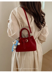 Close-up of a burgundy leather bucket bag with gold buckle and a cute teddy bear charm