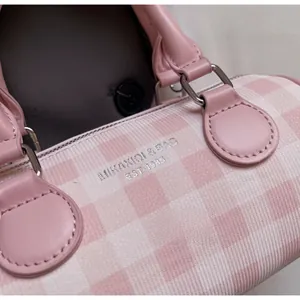 Gros plan du sac cylindre à carreaux roses et blancs avec poignées en cuir et surpiqûres