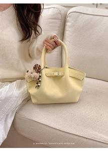Detail of cream pleated bucket bag featuring a gold buckle and cute puppy plush charm