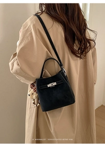 Detail of black suede bucket bag with silver lock and a cute bear charm on a trench coat