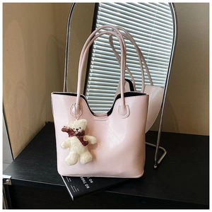 Detail of light pink patent leather tote bag with a cute plush bear charm on a black desk