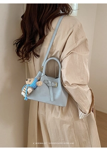 Detail of light blue bucket bag with cute bear charm and leather strap on a model