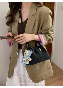 Detail of a minimalist black leather bucket bag with cute bear charm on a model