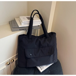 Detail of a large black tote bag with double straps and front flap pocket on a stool