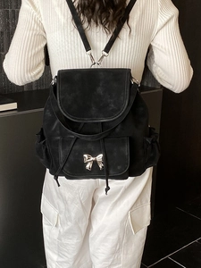 Black matte backpack with silver bow decoration and drawstring closure on a model
