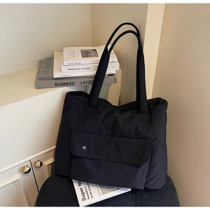 Detail of a large black nylon tote bag with pocket and metal buttons on a soft surface