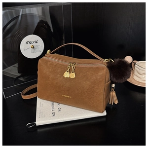 Detail der braunen Vintage-Kissentasche mit goldenen Doppelreißverschlüssen und Plüsch-Anhänger