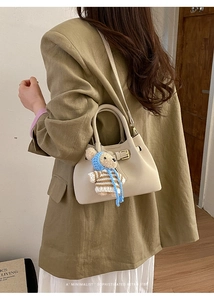 Detail of cream retro bucket bag with gold buckle and cute brown bear charm