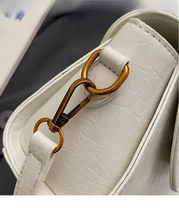 Gros plan détaillé de la quincaillerie en bronze sur un sac en cuir grainé blanc chic