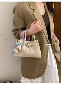 Detail of cream beige bucket bag with metal buckle and cute bear plush charm