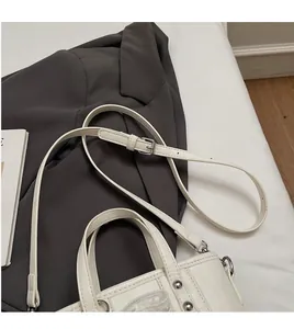 Dettaglio borsa a secchiello beige con tracolla regolabile e borchie metalliche argento