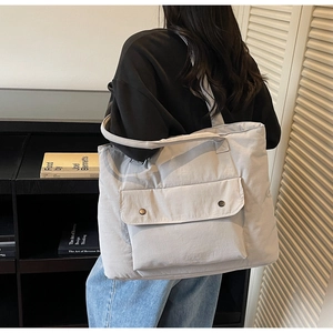 Detail of light grey quilted tote bag with magnetic front pocket shown on a model back
