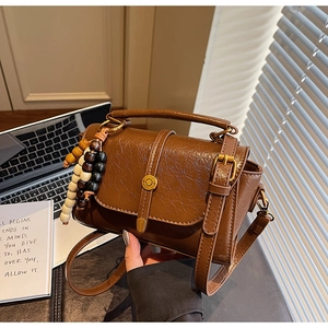 Détail du sac bandoulière marron rétro avec charme en perles de bois sous une lumière douce