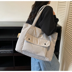Close-up of light gray quilted nylon tote bag with large front pocket and black snap buttons