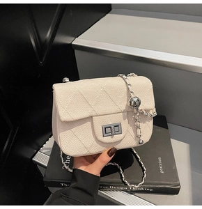 Detail of cream woven quilted shoulder bag featuring silver clasp and chain strap