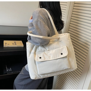 Close-up of off-white canvas tote bag featuring a front pocket with black snap buttons